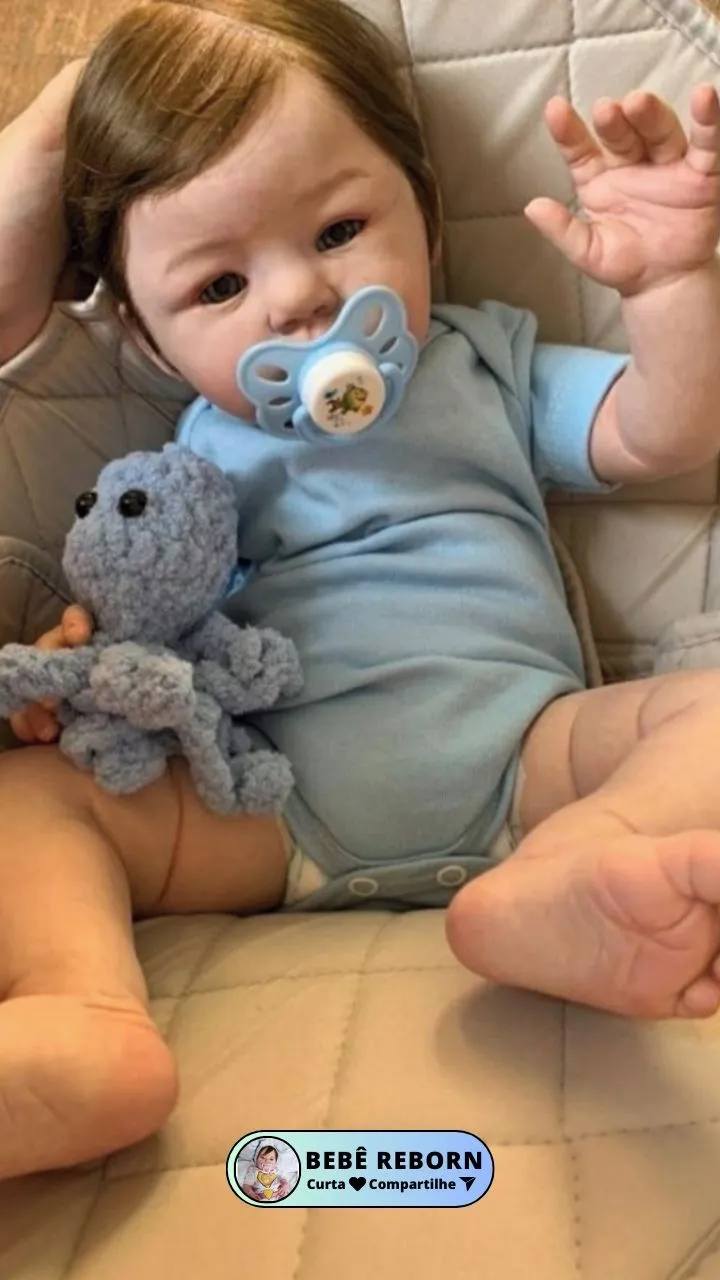 Imagem do bebê reborn henrico sentando com uma roupinha azul